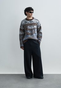 Sweter dziany z niebieskim, brązowym i białym wzorem, okrągłym dekoltem i szerokimi rękawami. Połączony z szerokimi czarnymi spodniami.