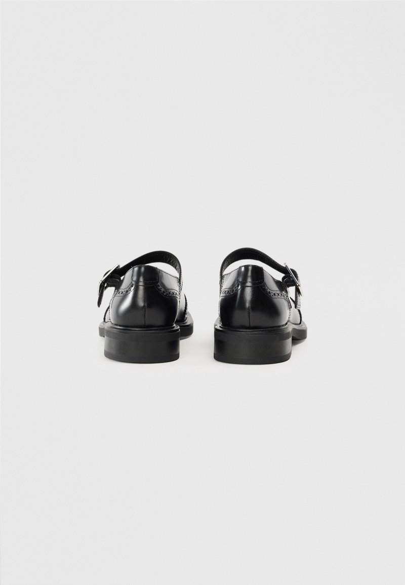 Chaussures en cuir noir avec un petit talon, une bride au dos et des perforations décoratives le long du bord. Texture lisse avec une finition brillante.