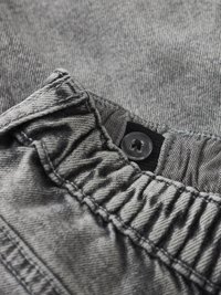 Tejido de mezclilla gris con cinturilla elástica fruncida, con un botón negro y detalles de costura. Vista en primer plano de la textura.