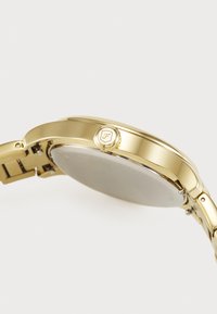 Montre en métal doré avec une finition polie, boîtier rond et couronne proéminente. Le bracelet est composé de segments métalliques liés pour un ajustement réglable.