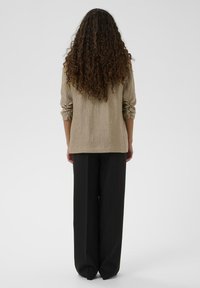 Haut beige texturé à manches longues avec des manches retroussées, associé à un pantalon large noir taille haute. L'accent est mis sur la vue de dos.