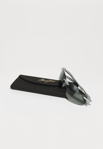 Des lunettes de soleil avec monture grise et verres foncés reposant sur un étui noir. L'étui présente une inscription dorée. Design léger et minimaliste.