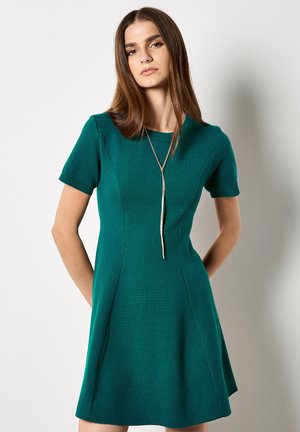 Vestido verde de manga corta hecho de tejido de punto, con un corsé ajustado y una falda acampanada, con un escote redondo y costuras visibles.