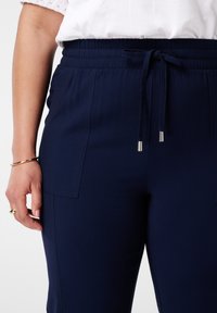 Pantalons bleu marine avec une taille élastique, fermeture à cordon et poches latérales en biais. Texture lisse et design ajusté avec des coutures discrètes.