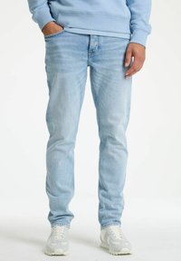 Svetlo modri kavbojki z ozkim krojem in rahlo obrabljenim videzom; vsebujejo tradicionalni dizajn s petimi žepi in gladko teksturo.