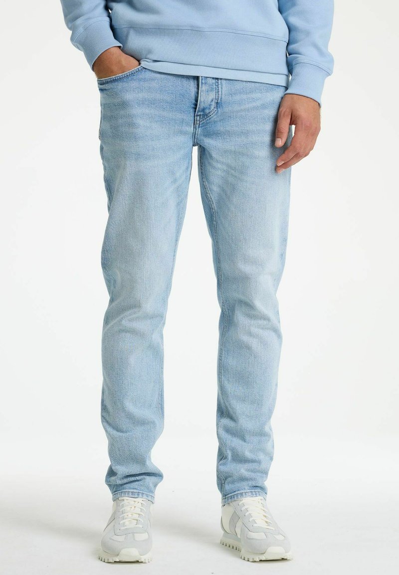 Svetlo modri kavbojki z ozkim krojem in rahlo obrabljenim videzom; vsebujejo tradicionalni dizajn s petimi žepi in gladko teksturo.