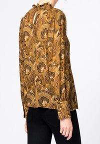 Blouse à manches longues dans un motif paisley brun doré avec un dos en keyhole et un col froncé. Fabriquée en tissu léger, elle présente des poignets élastiques.