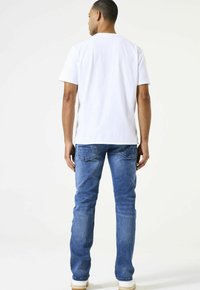 Camiseta blanca de algodón combinada con jeans de mezclilla azules. Los jeans tienen un diseño clásico de cinco bolsillos y sutiles acentos desgastados.