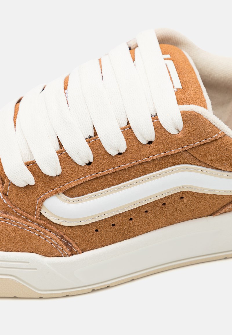 Brązowe zamszowe sneakersy z białymi sznurówkami, z białym paskiem po boku i perforacjami na cholewce zapewniającymi wentylację. Teksturowana podeszwa.