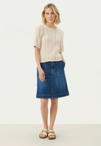 Haut en tricot beige à manches courtes avec col rond et détail de boutons, associé à une jupe en denim bleue avec poches et un ourlet subtil.