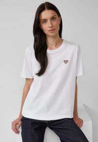 T-shirt en coton blanc à manches courtes et col rond, avec un petit cœur coloré brodé sur la poitrine.
