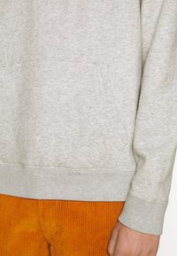 Lichtgrijze sweatshirt met een voorzak, textuurstof en geribde manchetten, gecombineerd met oranje corduroy broeken.