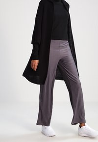 Cardigan nero lavorato a maglia con colletto, abbinato a pantaloni grigi plissettati e sneakers bianche. Il cardigan ha un'apertura frontale e maniche ampie.