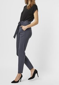 High-waisted trousers in dark gray fabric, featuring a tie belt, side pockets, and tapered design, paired with black pump shoes.