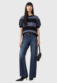 Maglione a righe in navy e grigio, abbinato a jeans blu a vita alta. Scarpe nere a punta e una piccola borsa nera completano il look.