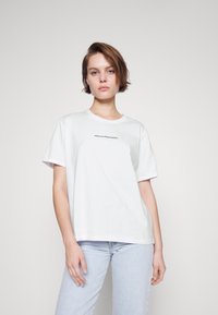 White cotton T-shirt with short sleeves, relaxed fit, featuring black text "MSCHCOPENHAGEN" on the front. Worn with light blue jeans.