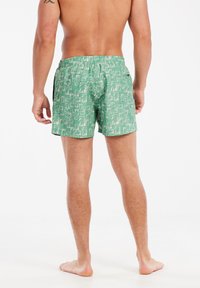 Gröna badshorts med ett vitt palmbladsmönster, elastisk midja och avslappnad passform. Materialet verkar lätt och texturerat.