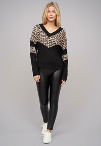 Fekete és bézs kötött pulóver geometrikus mintával, V-nyakkal, hosszú ujjakkal, fekete leggings-szel és fehér tornacipővel párosítva.