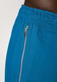 Shorts en coton bleu avec une taille élastique, dotés d'une fermeture éclair argentée sur le côté pour un ajustement et une texture lisse.