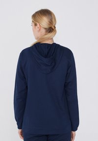 Sudadera azul marino de tejido suave, con capucha ajustable, mangas largas y puños acanalados. Diseño sencillo sin patrones.