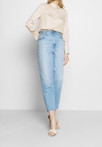 Beige button-up shirt with a grid pattern, high-waisted light blue jeans, and beige heeled sandals, displayed against a plain background.
