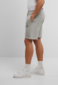 Grijze elastische tailleband shorts met zijzakken en een logo nabij de heup. Gecombineerd met witte sneakers en enkelsokken. Glad textuur.