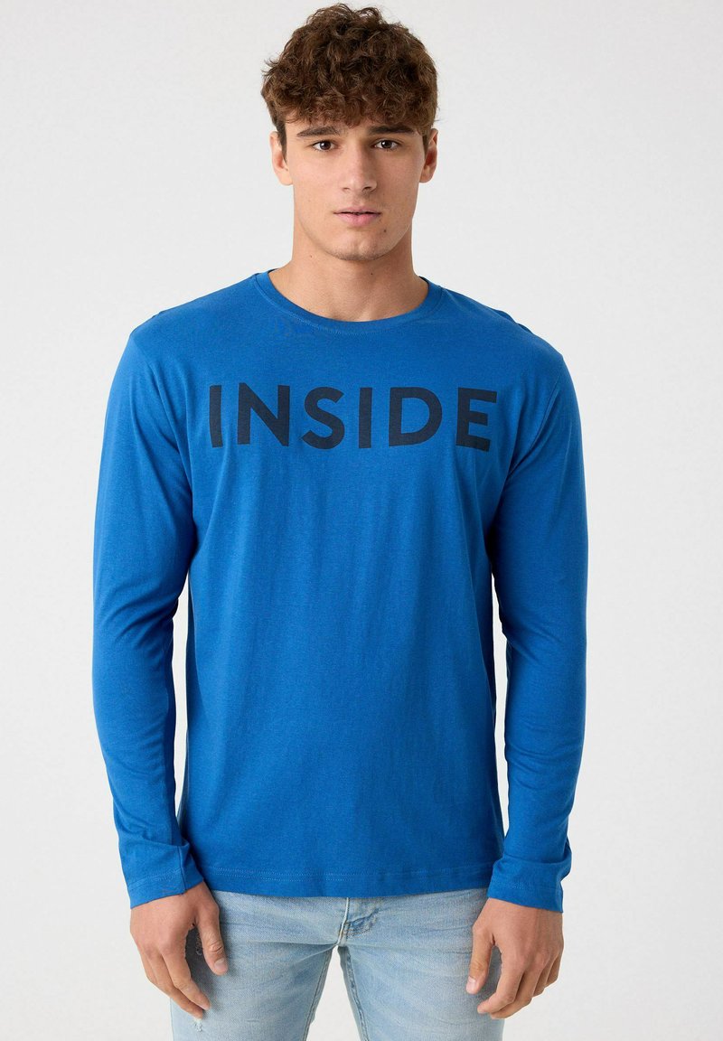 Camiseta de manga larga azul hecha de un tejido suave, que presenta la palabra "INSIDE" en letras negras en negrita en la parte frontal.