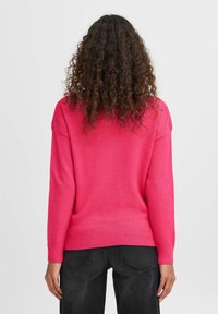 Pull en tricot fuchsia avec des poignets et un ourlet côtelés. Offre une coupe décontractée et des épaules larges. Porté avec un jean sombre.