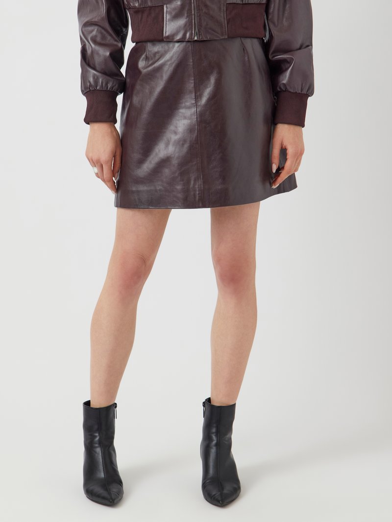Bordeaux leren minirok met een gladde textuur en een getailleerd silhouet, gecombineerd met zwarte leren enkellaarzen met een spitse neus.