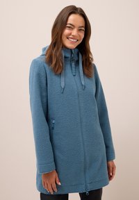 Veste en polaire bleue avec capuche, dotée d'une fermeture éclair sur le devant, d'accents à cordon de serrage et d'une finition texturée. Manches longues et poches latérales.