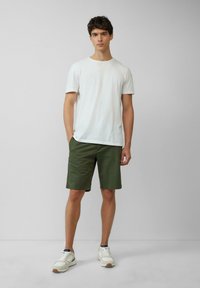 T-shirt en coton blanc, shorts verts et baskets blanches avec des détails gris clair ; le T-shirt a un col rond et une coupe décontractée.