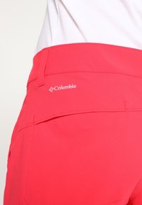 Růžové šortky Columbia s hladkou texturou, s kapsou na zadní straně a logem. Navrženy pro pohodlí a venkovní aktivity.