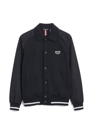 Veste noire à boutons avec col, deux poches latérales, poignets et bas élastiques avec rayures blanches, et un petit patch logo sur la poitrine.