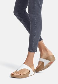 Sandali wedge bianchi e beige con una fascia ampia e design open toe; suola testurizzata e materiale morbido per il comfort. Indossati con jeans scuri.