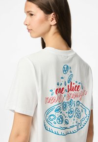 Vit bomullströja med blå och röd grafisk tryck av en pizza med texten "en skiva är aldrig nog" på ryggen.