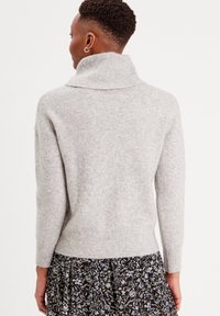 Suéter gris de punto con un cuello alto de canalé, mangas largas y un ajuste ceñido. La textura parece suave y ligeramente pelusa.