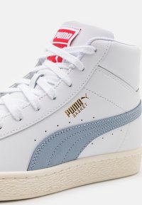 Bílé kožené vysoké tenisky s světlemodrými akcenty, texturovanou střední podrážkou a zlatým logem na boku. Červená etiketa na jazyku.