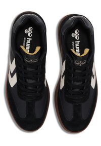 Chaussures de sport noires en suède et cuir, avec des bandes chevrons blanches, des lacets noirs et une semelle en caoutchouc marron.