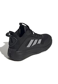 Chaussure de sport noire avec une tige en mesh, rayures blanches en accent et semelle en caoutchouc texturé. Dispose d'un col rembourré et d'une languette à l'arrière.