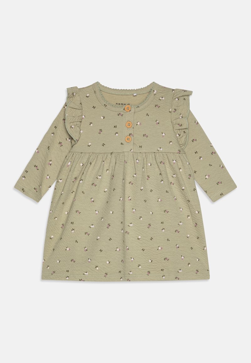 Grön bomullsklänning med långa ärmar, volangdetaljer på axlarna, blommönster och träknappar framtill. Dragsko i midjan.