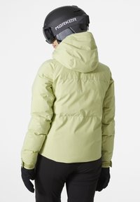 Hellegrüne Skijacke mit Kapuze, gesteppter Gestaltung und glatter Textur. Auch schwarze Handschuhe und ein Helm mit Branding sind sichtbar.