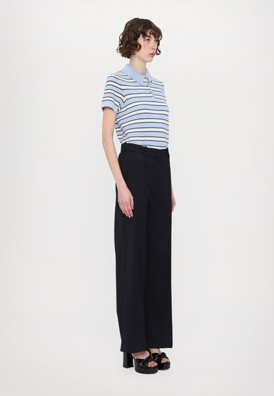 Gestreiftes Poloshirt in Hellblau und Marineblau, kombiniert mit hochtaillierten schwarzen Hosen. Modell trägt schwarze Plateausandalen.