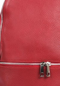 Roter Leder-Rucksack mit strukturierten Oberflächen, ausgestattet mit einem silbernen Reißverschluss und Zuglaschen, der ein kompaktes und strukturiertes Design betont.