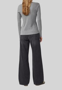 Woman with long hair wearing a fitted gray long-sleeve top and loose black wide-leg jeans, standing with her back to the viewer.