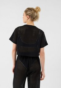 Zwarte mesh crop top met korte mouwen, voorzien van een geperforeerde textuur en een losse pasvorm. De achterkant heeft een afgeronde uitsnede voor extra ventilatie.