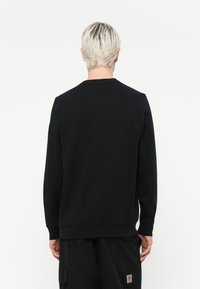 Sort sweatshirt med lange ærmer, rund hals og ribbede manchetter. Lavet af solidt stof, med et lille logo på venstre ærme.