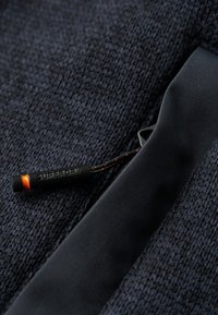 Tissu texturé bleu marine foncé avec un accent noir lisse, comportant une languette de tirage étiquetée "SUPERDRY" en noir avec une pointe orange, mettant en valeur le design.