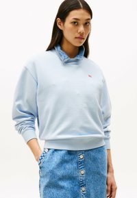Felpa azzurra con colletto in denim e polsini a coste. Logo prominente sul petto. Abbinata a una gonna in denim con bottoni frontali.