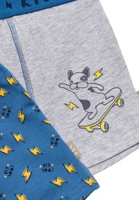 Ropa interior infantil gris y azul con cintura elástica. El par gris presenta un gráfico de un perro patinador; el par azul tiene patrones de relámpagos amarillos.