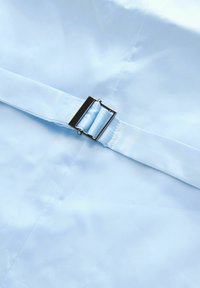 Helles blaues Gewebe mit glatter Textur, versehen mit einer rechteckigen silbernen Schnalle und einem passenden Riemen. Fokus auf klare Linien und minimalistisches Design.
